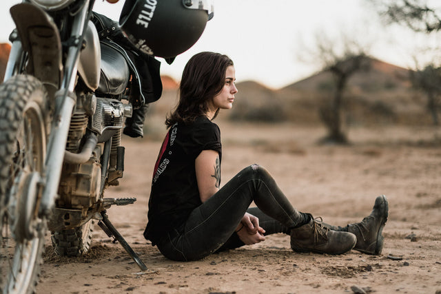 A woman sits in a desert next to a motorbike