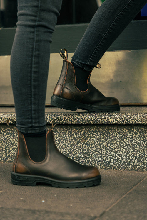 Two people wearing dark brown leather Chelsea boots and black skinny jeans are stepping on granite steps, with only their lower legs and feet visible.